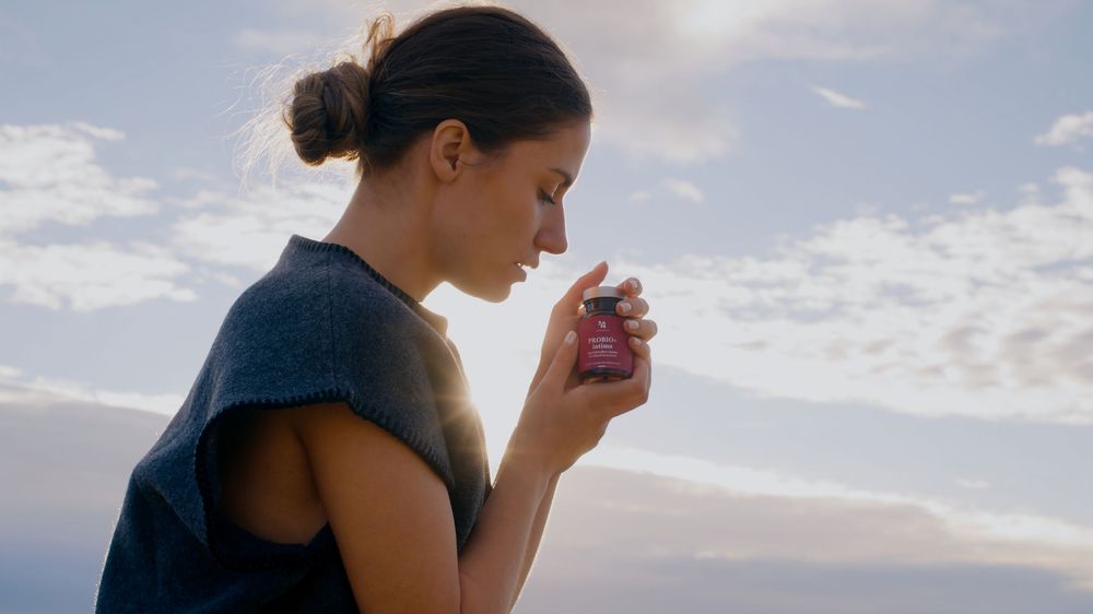 A person in a sleeveless top holds a cup while standing against a cloudy sky at sunset.