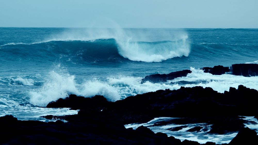 Dramatic aerial view of powerful ocean waves crashing against rugged rocky coastline during stormy weather.