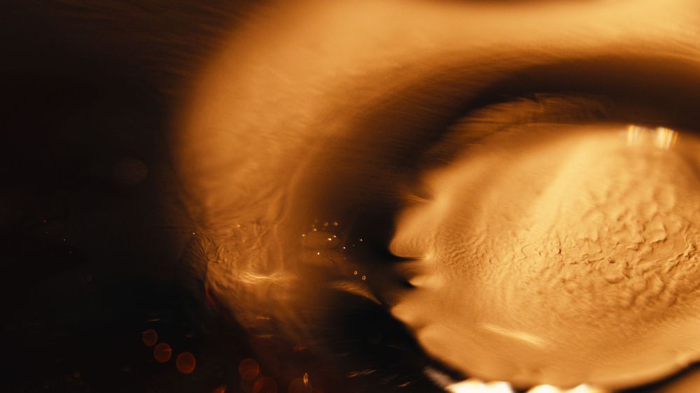 Abstract golden-brown swirls and curves create a fluid pattern in dark lighting.
