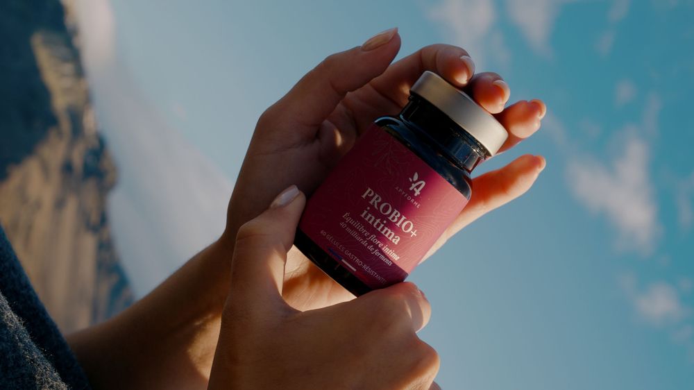 Hands holding up various skincare product bottles against a bright blue sky with white clouds.