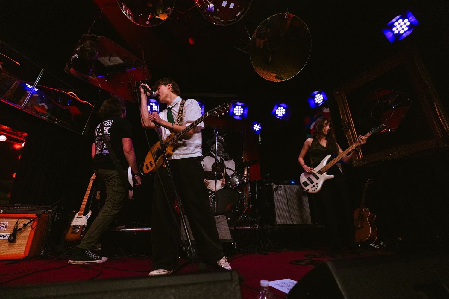 Rock band performs energetically on stage under blue lights with guitarist and bassist in a live music venue.