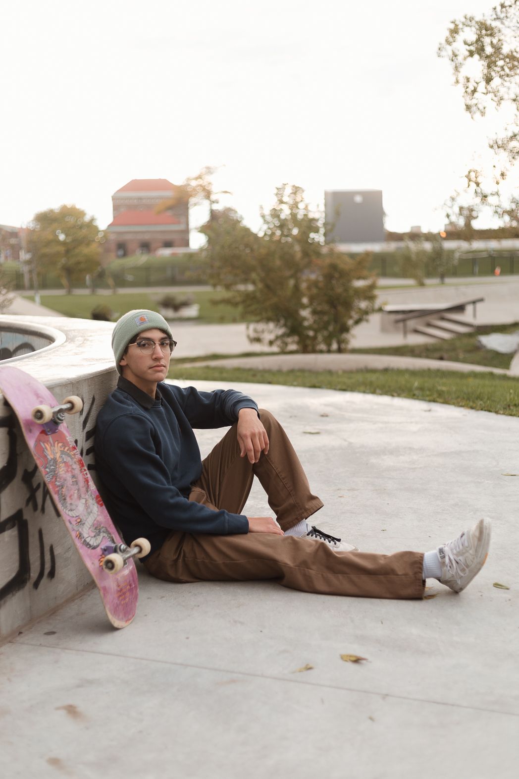 A skateboarder in casual wear relaxes against a concrete wall at a skate park.