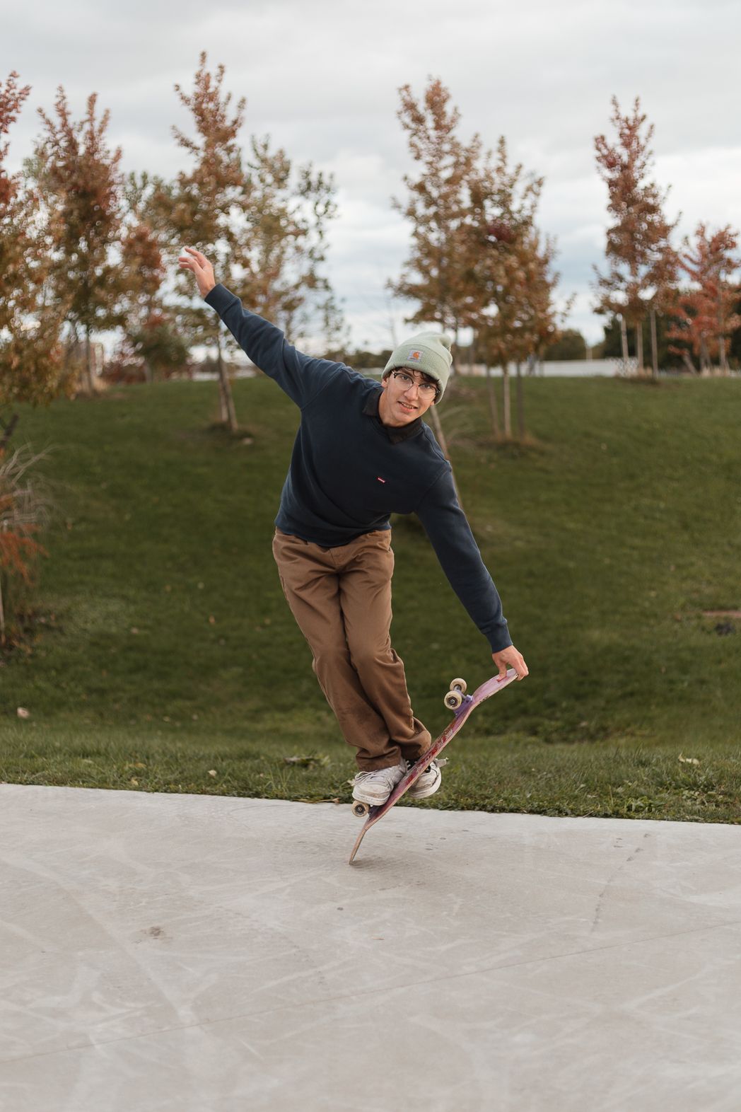 A skateboarder performs a trick on a concrete surface surrounded by autumn trees.