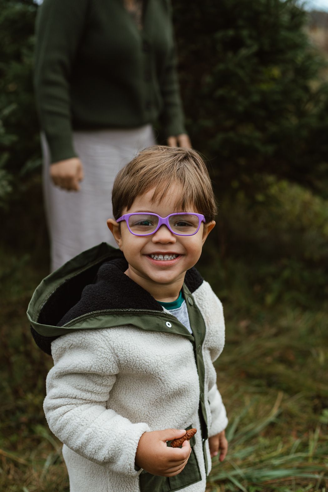 Child wearing purple glasses and white fleece smiles brightly at the camera.