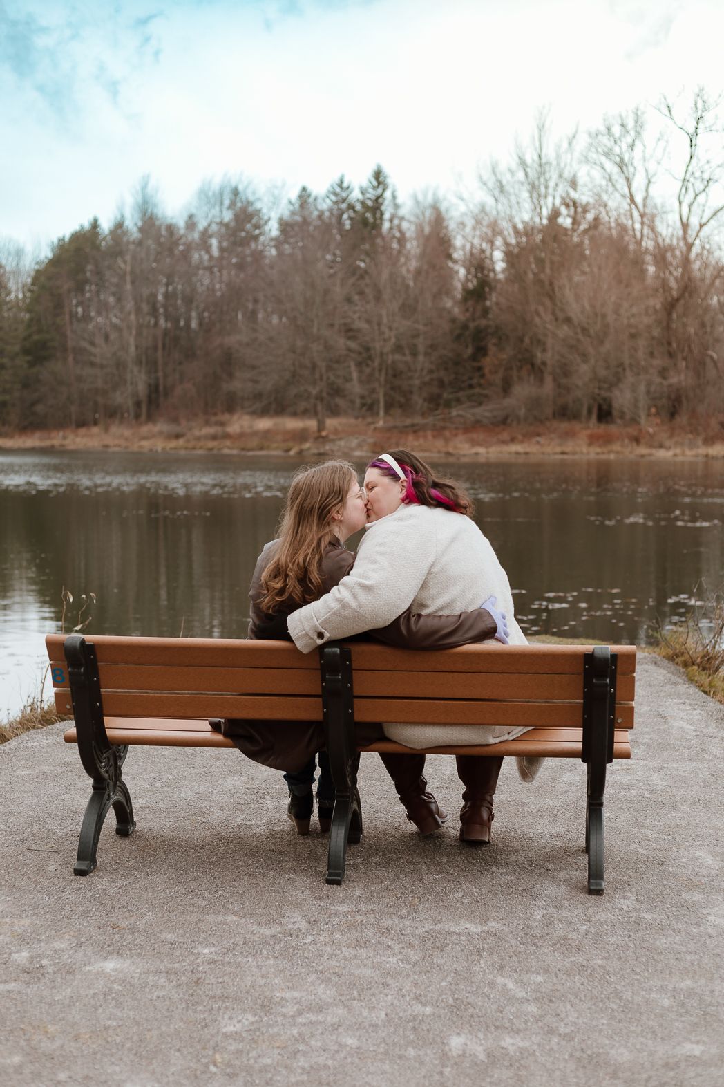 Couple sharing intimate moments while sitting on a park bench by a serene lake.