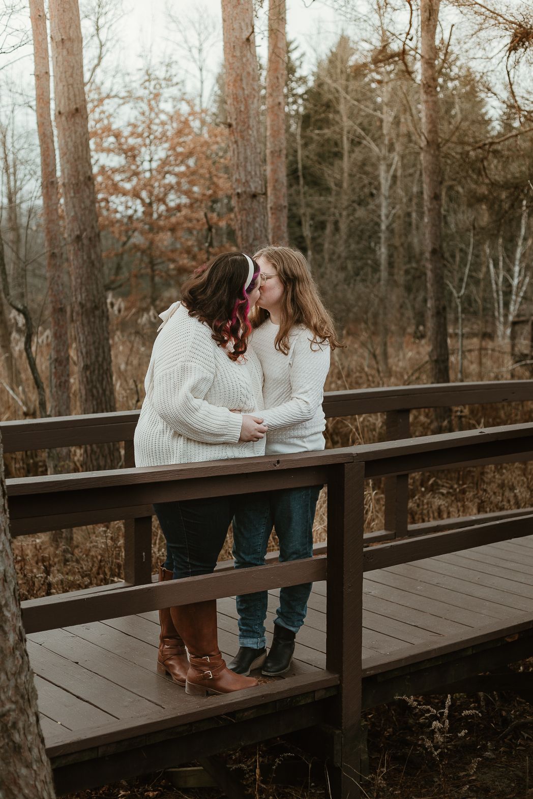 A couple shares romantic moments on a wooden boardwalk surrounded by autumn trees.