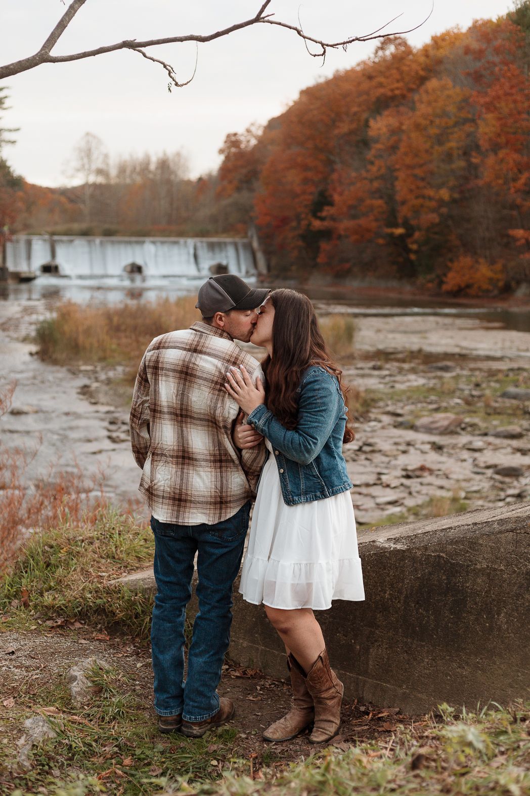A romantic autumn photoshoot by a rocky riverbank with fall foliage in the background.