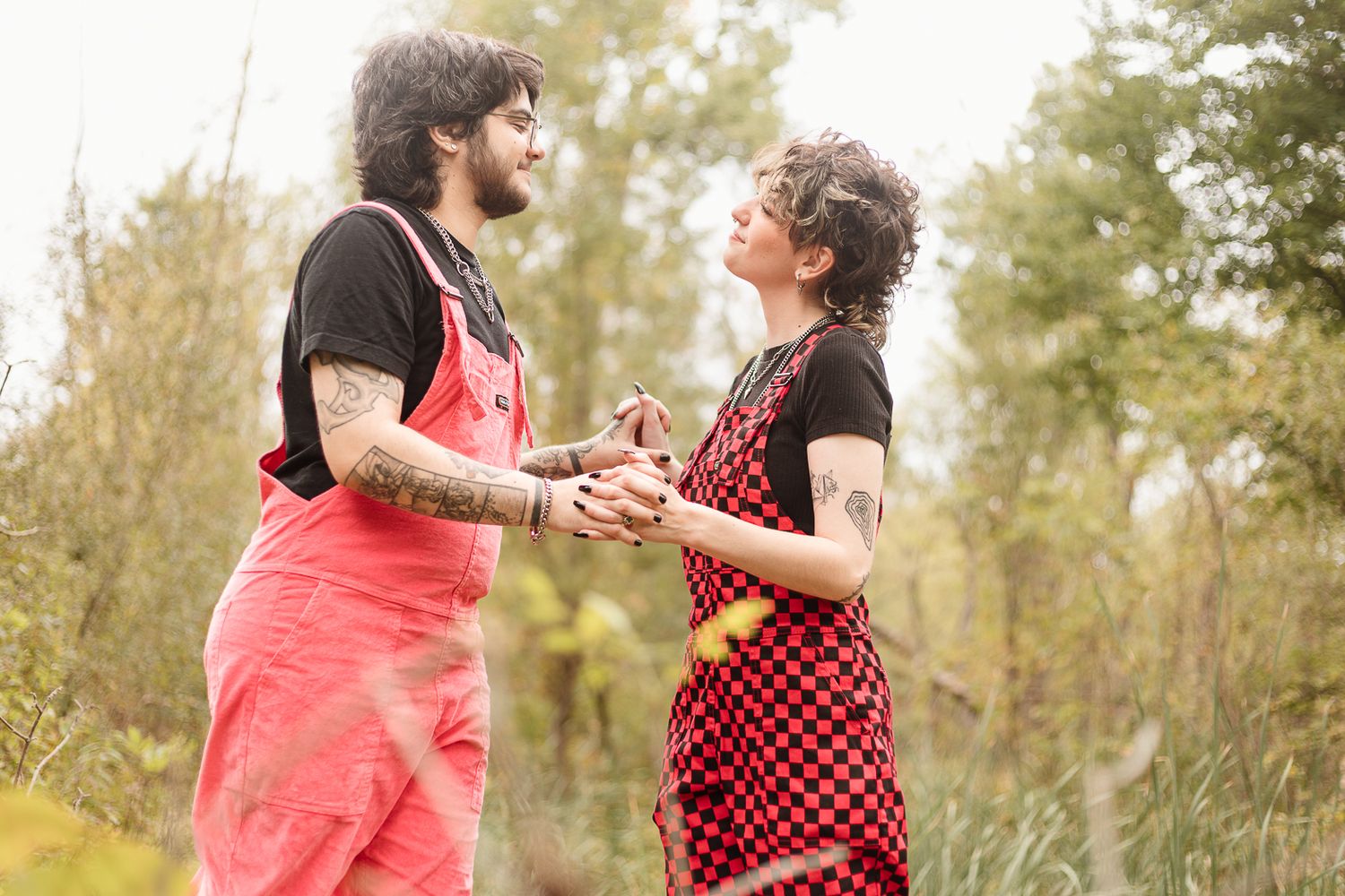 Two people in contrasting outfits dance joyfully in a wooded setting.