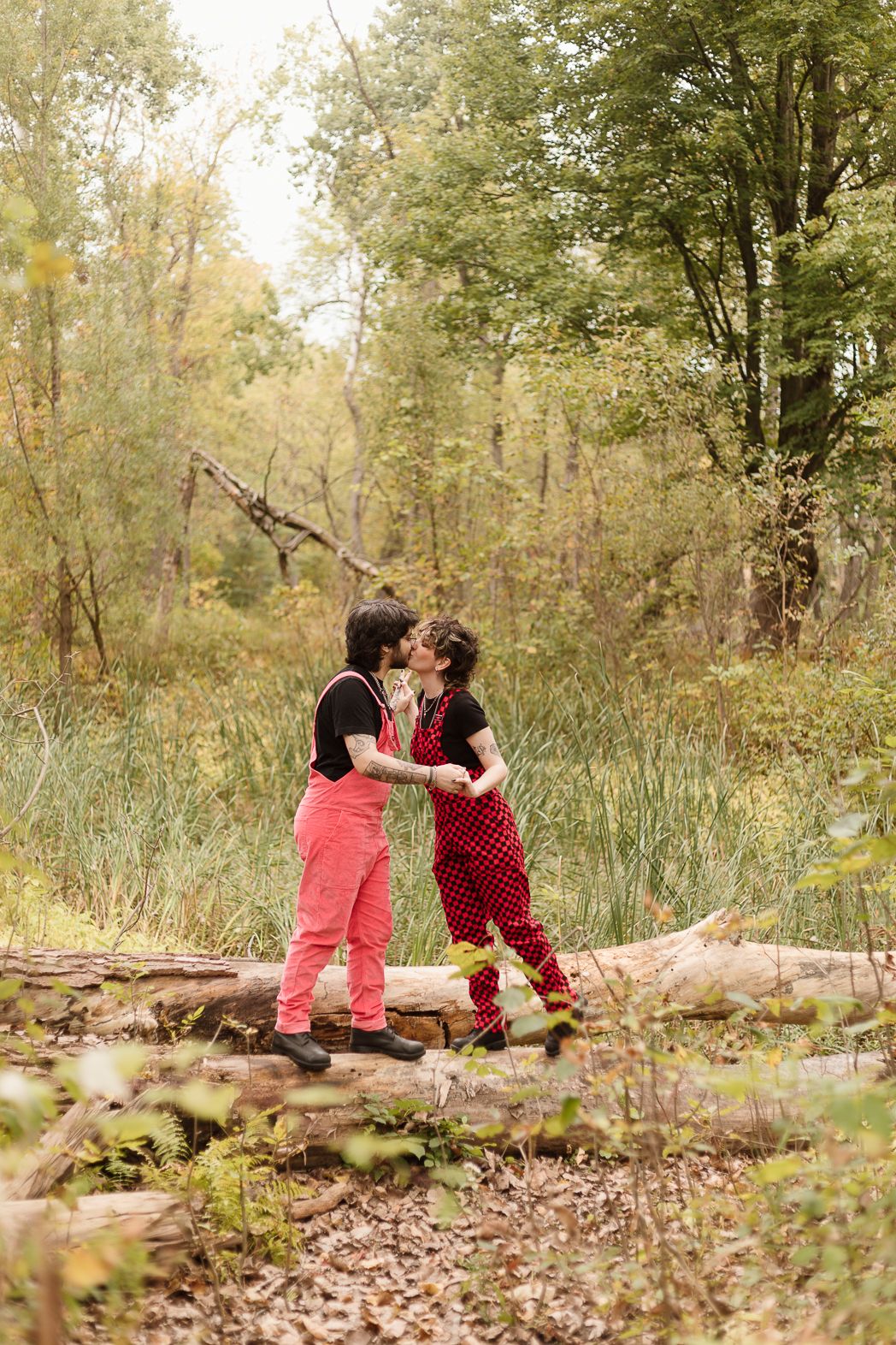 A romantic forest scene with two people in bright clothing embracing on a fallen tree.