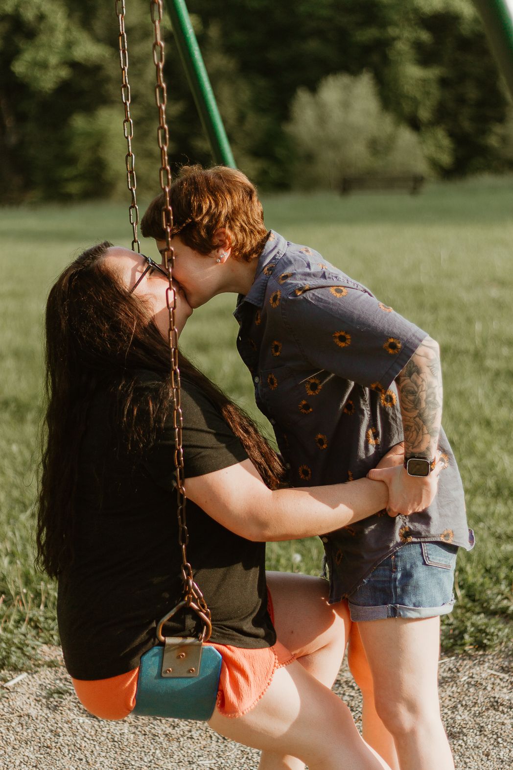 Couple sharing intimate moment on outdoor swing set during golden hour.