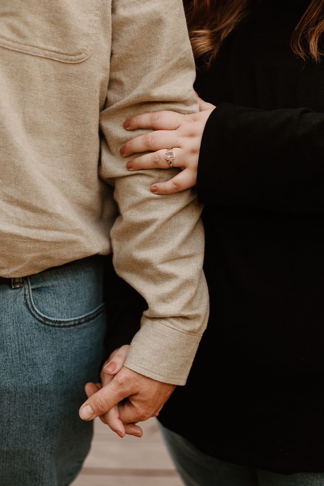Close-up view of intertwined hands wearing casual clothing with beige sweater and denim jeans.