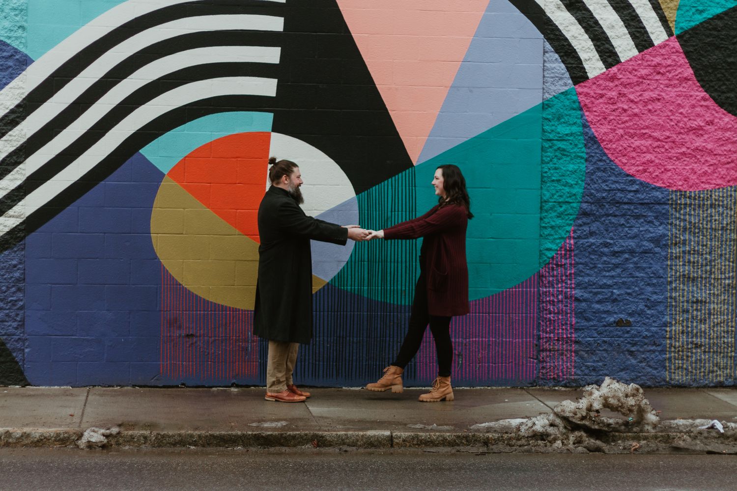 Two people standing in front of colorful geometric mural wall art.
