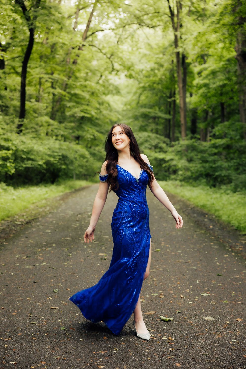 Prom mini session senior twirls in a sparkly blue formal dress on a wooded path.