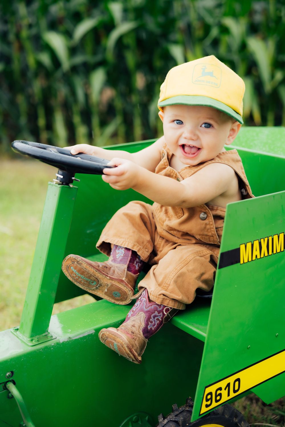 Toddler smiling while playing in a green toy tractor outdoors.