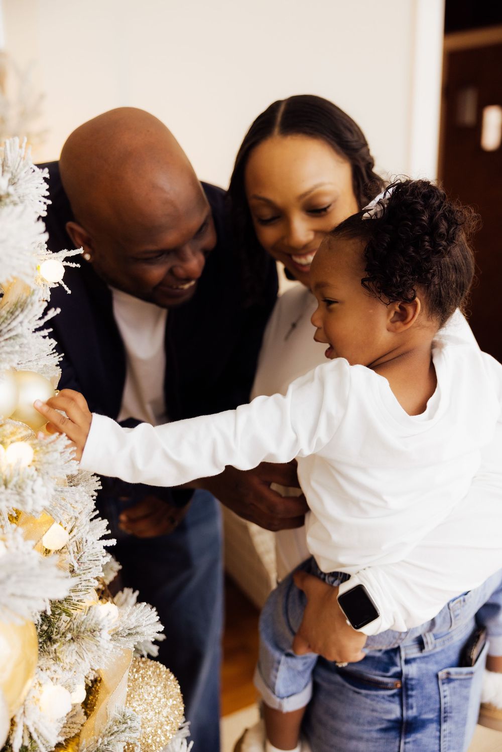 Intimate family portrait with white sweaters and denim against holiday decorations.