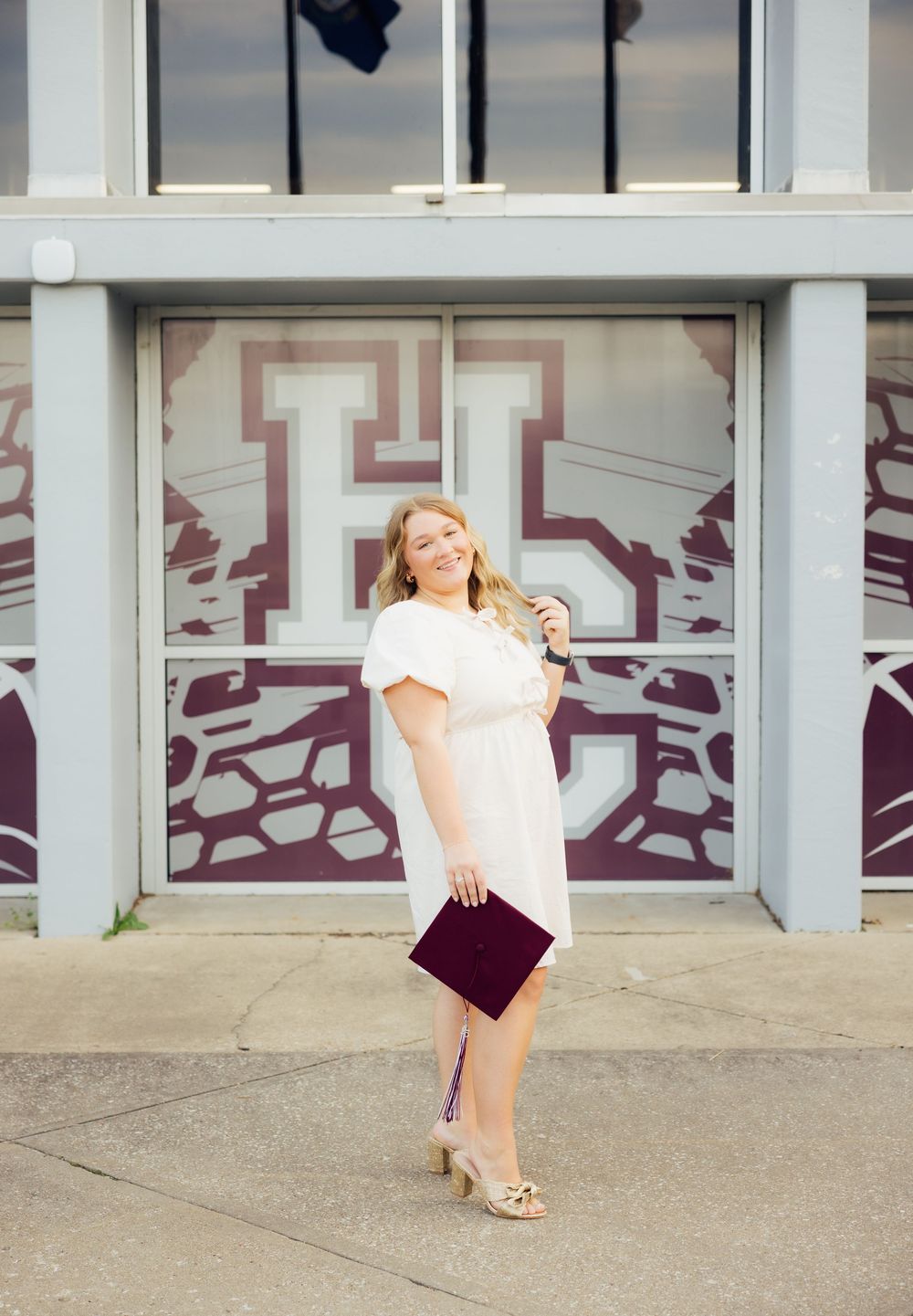 Graduate posing playfully outside their high school building.