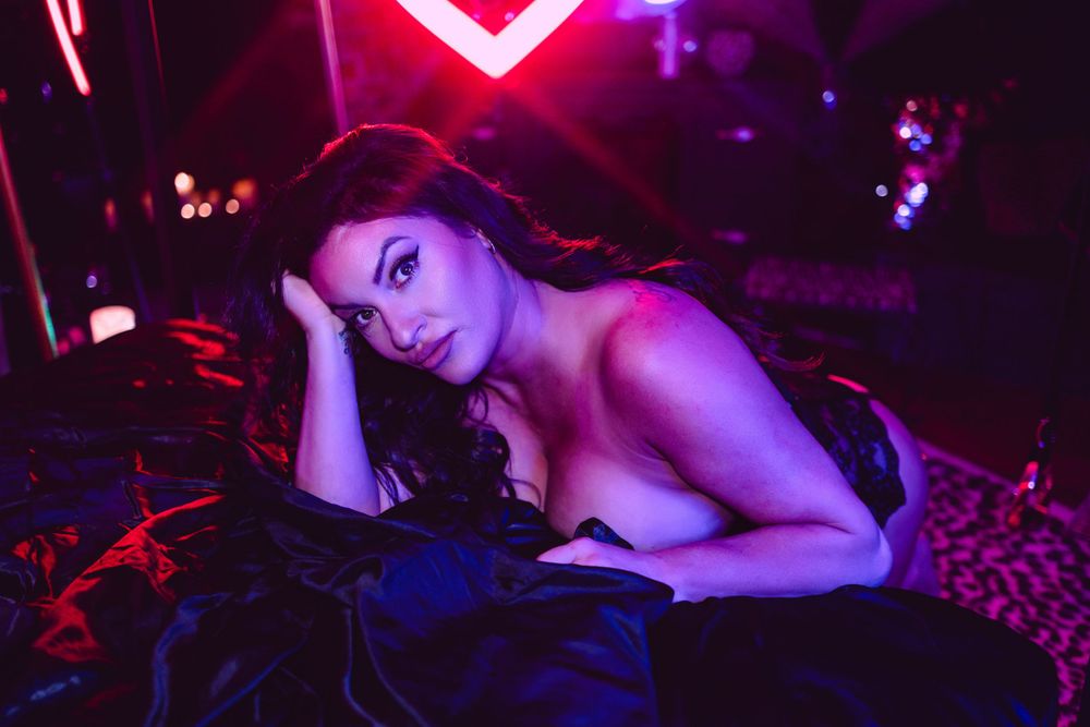 A dramatic nightclub scene bathed in pink and red neon lighting creates a moody atmospheric portrait.