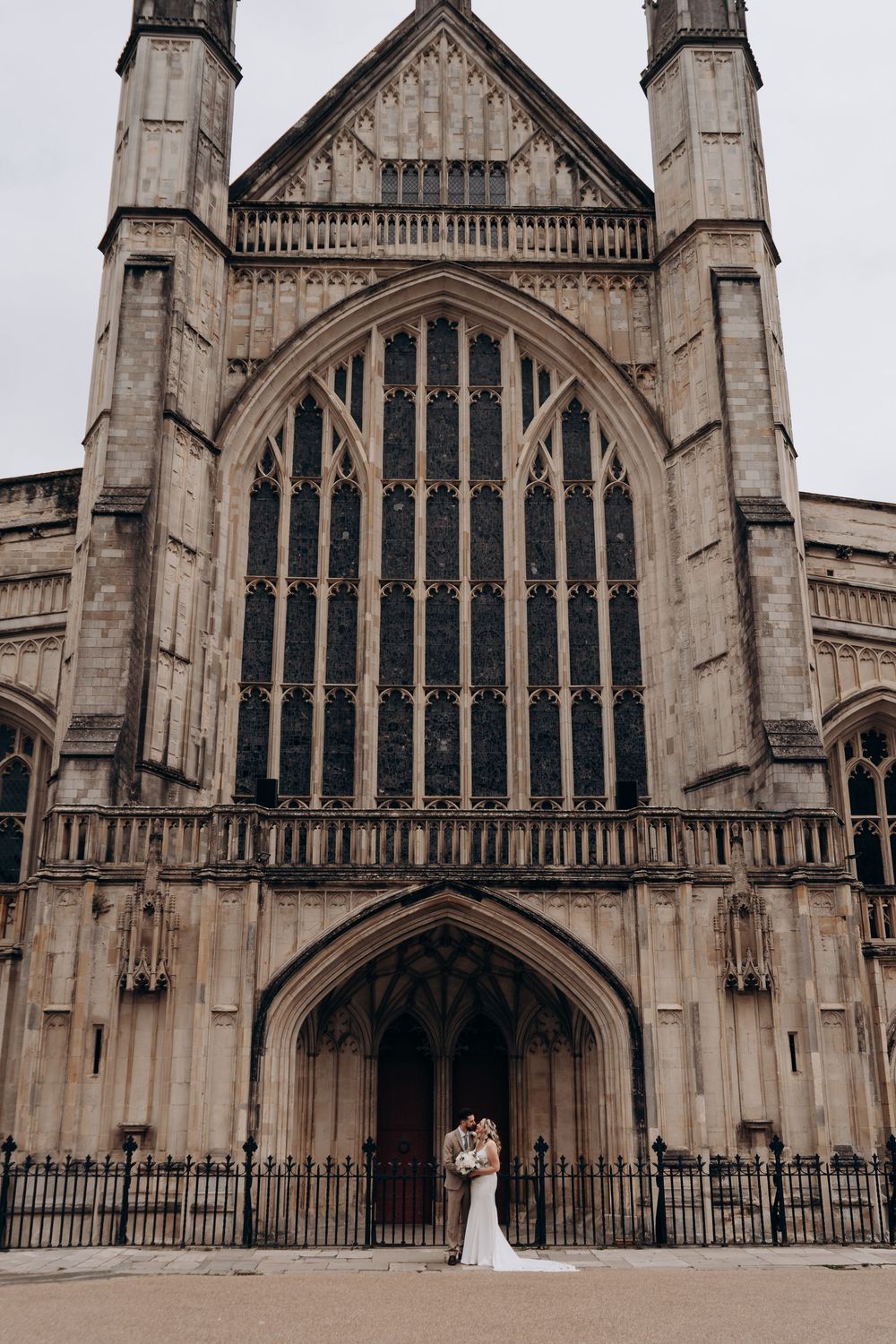 Bride and groom embracing before grand Gothic cathedral entrance with ornate arched windows on their wedding day.