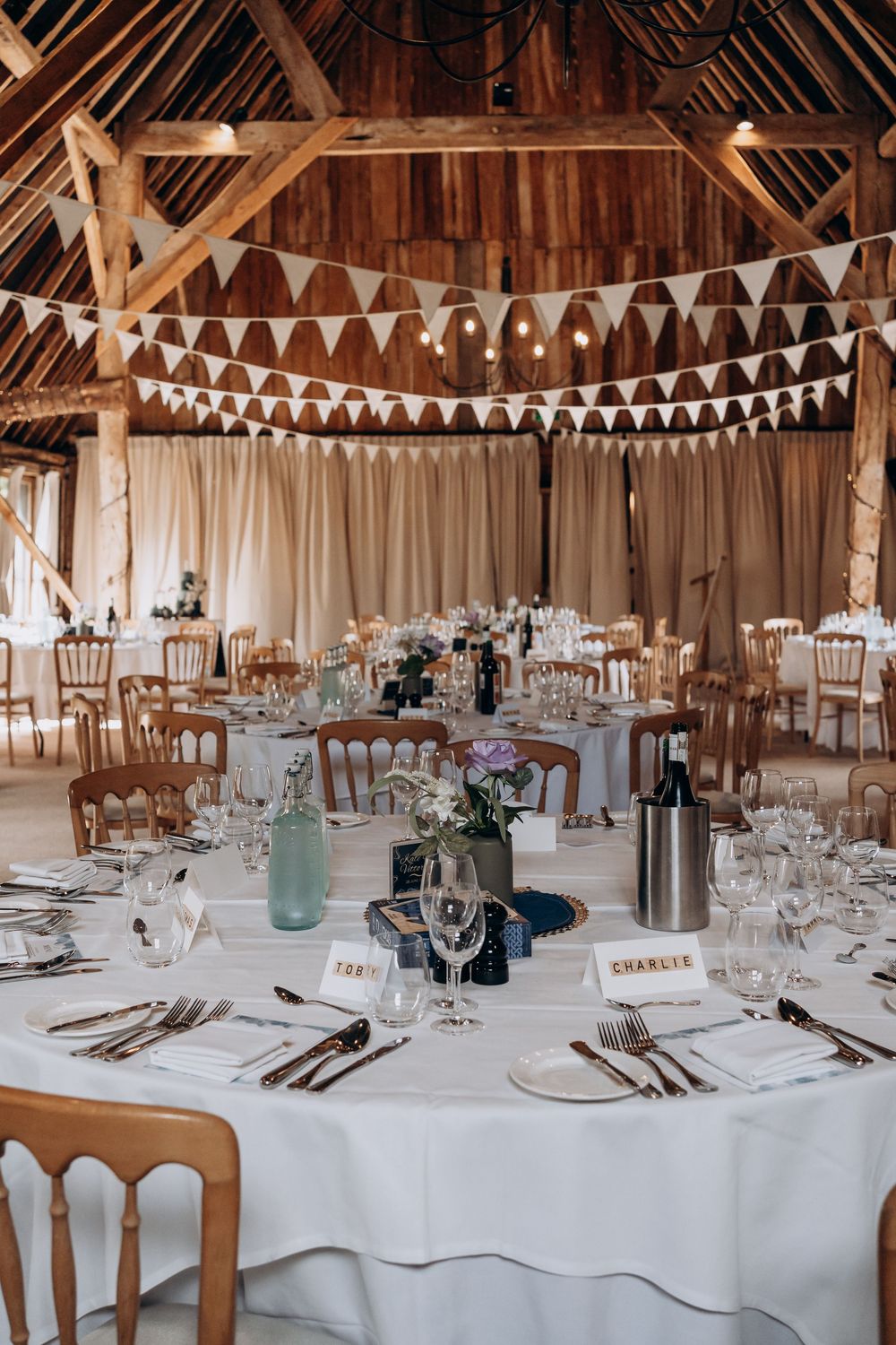 Rustic barn wedding reception with round tables, white linens, bunting, and elegant place settings.