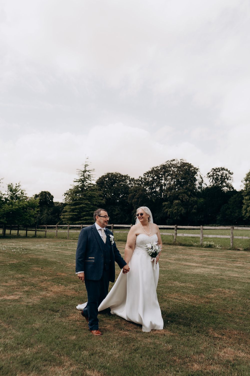 Bride and groom walk hand in hand across a lush green lawn at an outdoor wedding venue.