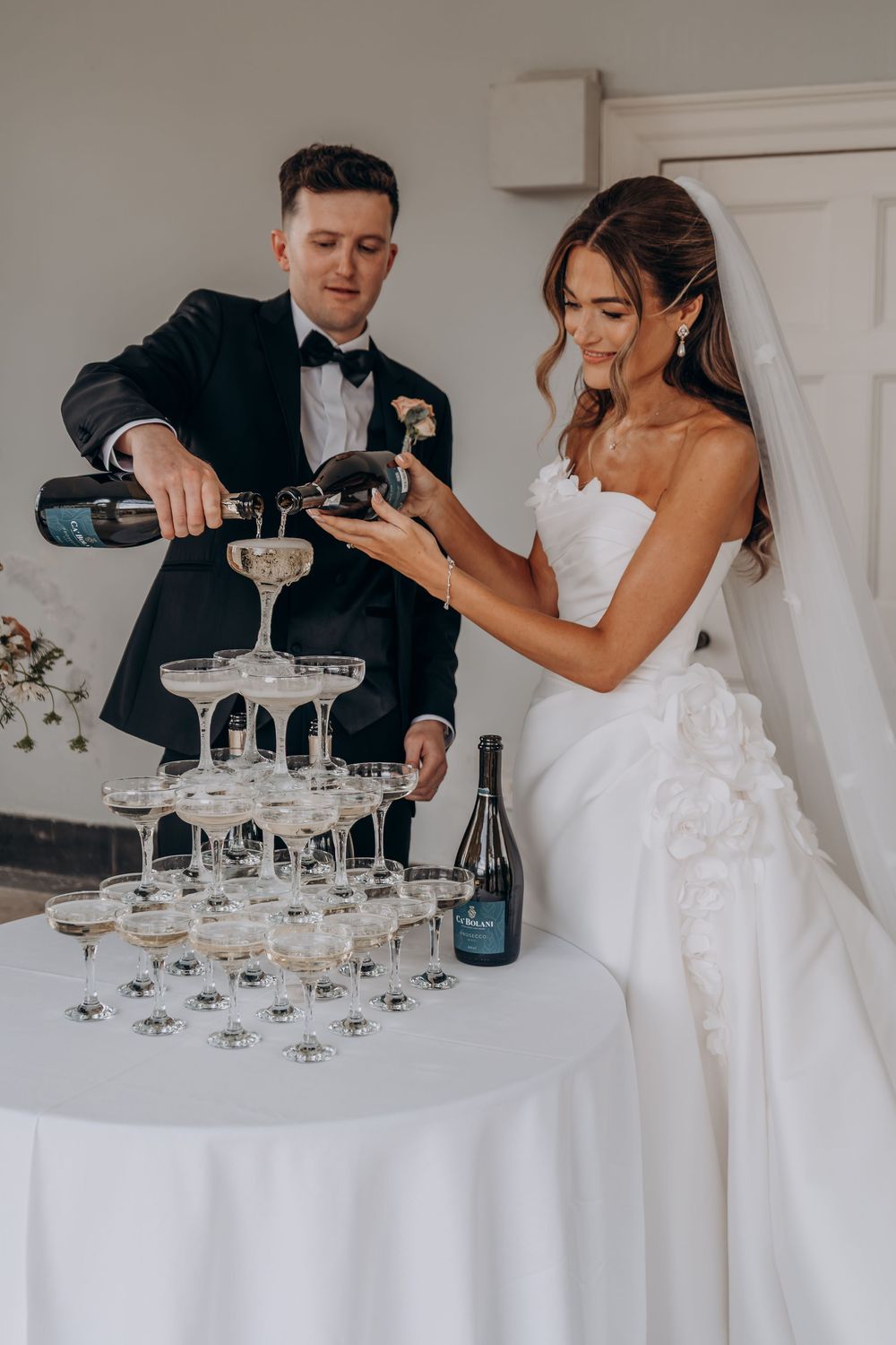 Bride and groom pouring champagne tower at wedding reception, elegant white gown and black tuxedo.