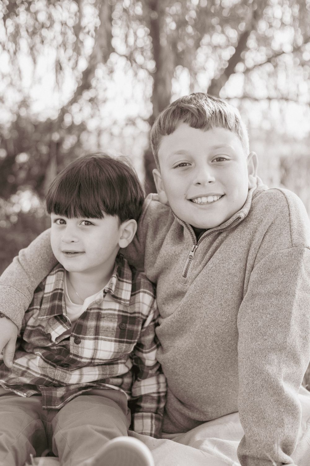 Black and white photo series of two children in casual clothing sitting together and smiling outdoors.