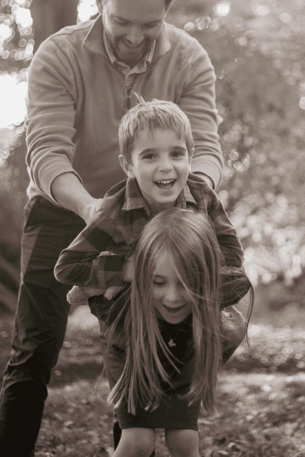 Black and white candid photos show joyful family moments playing and laughing together outdoors.
