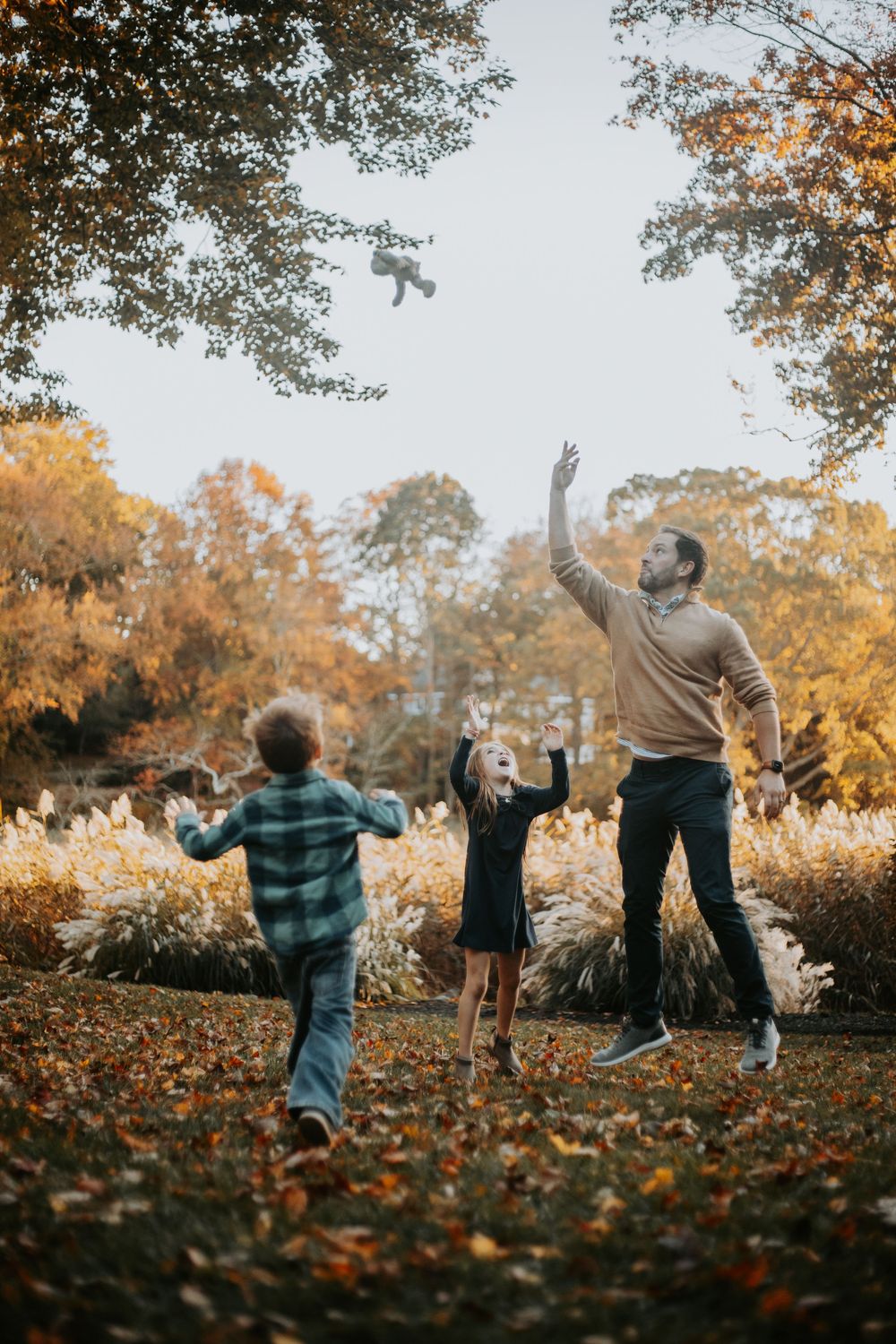 A sequence of silhouettes throwing autumn leaves in the air during golden hour in a park setting.