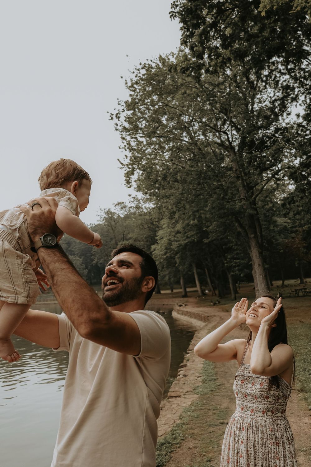 Family enjoying playful moments together near a serene lake in a park setting.