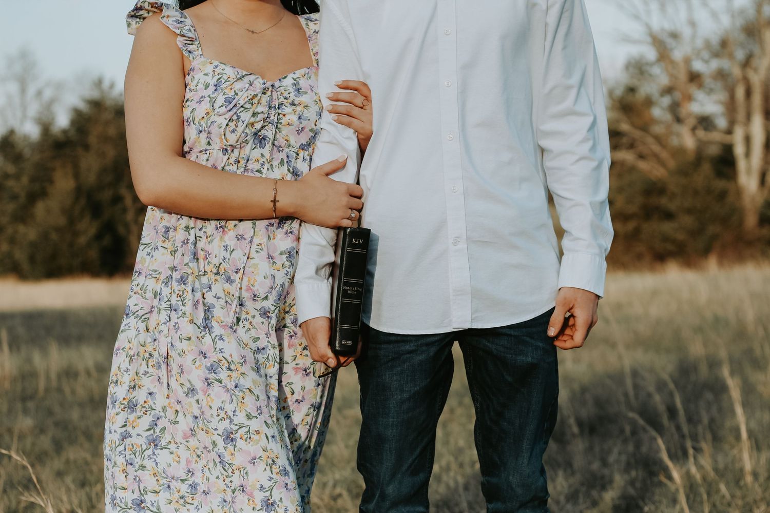 A couple in casual attire share a tender moment in a sunlit field.