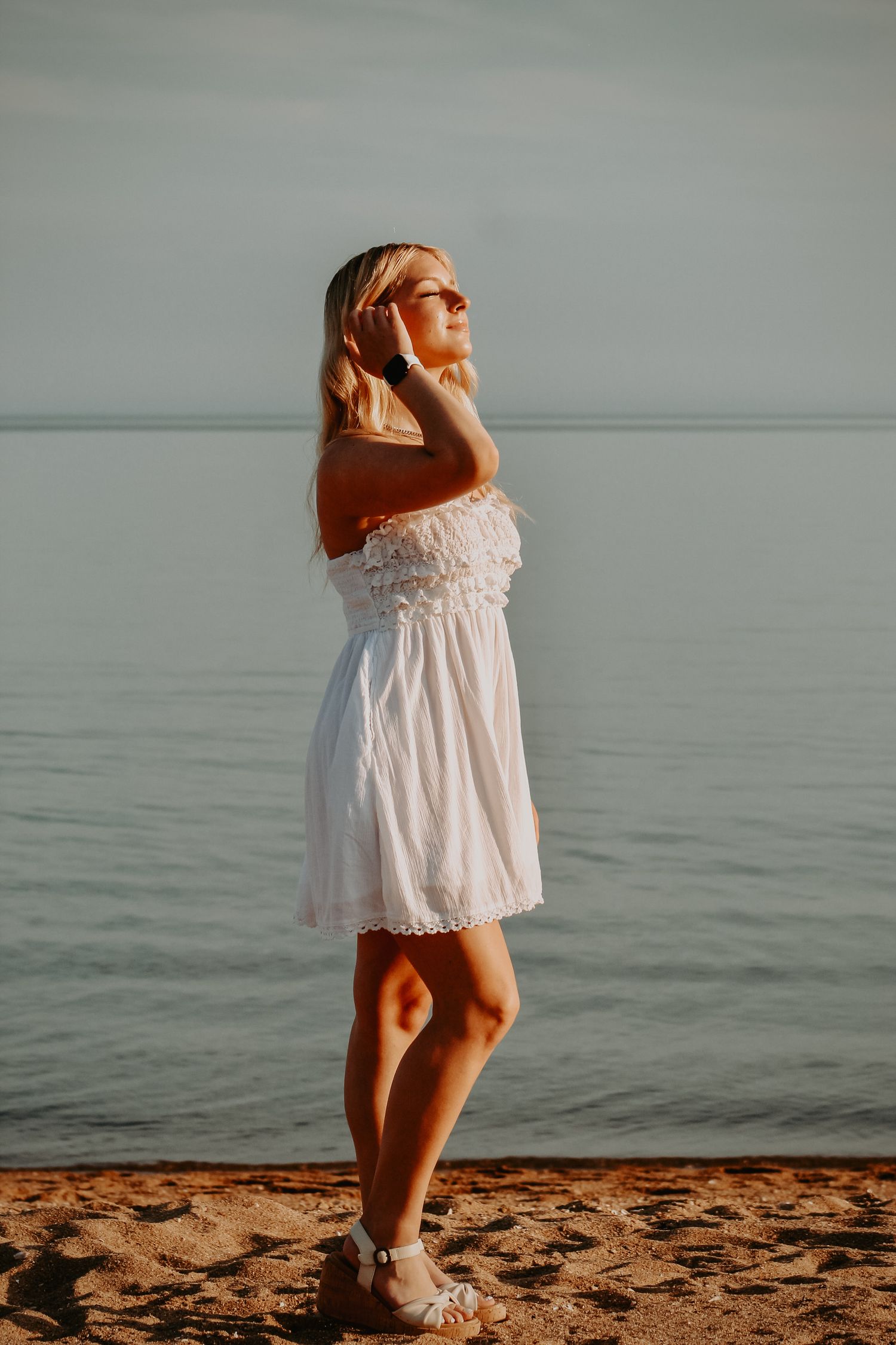 A white sundress is illuminated by golden sunlight on a beach at sunset.