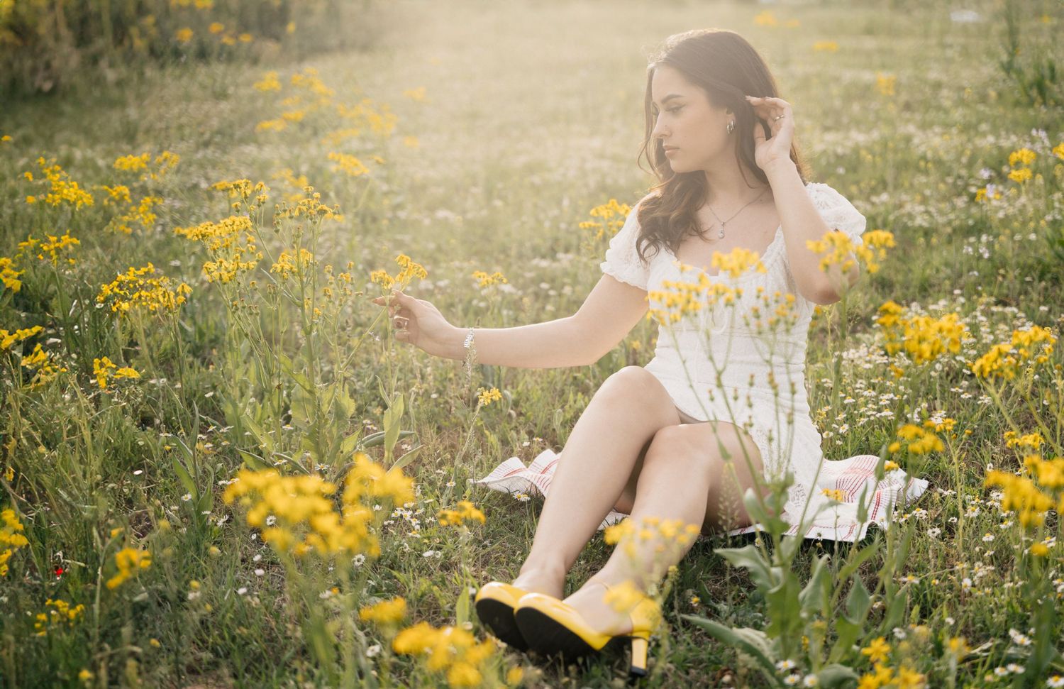 Person in white dress and yellow boots sitting among wildflowers in a sunny meadow.