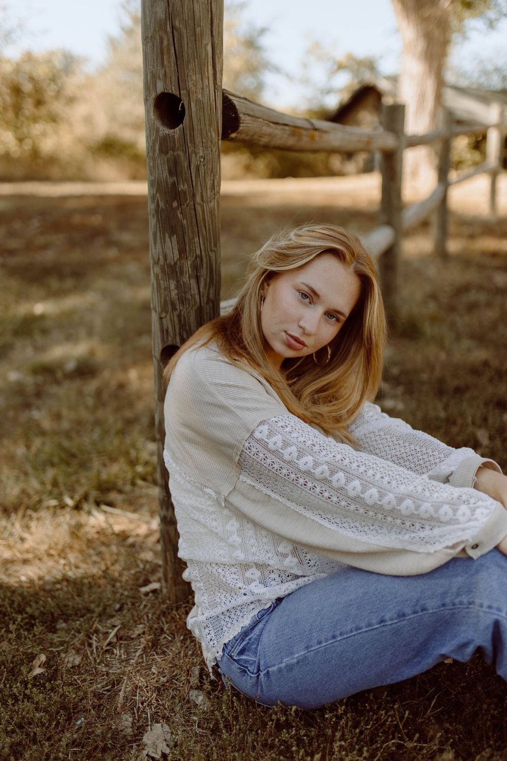 Rustic outdoor portrait against weathered wooden post in white lace top and jeans.