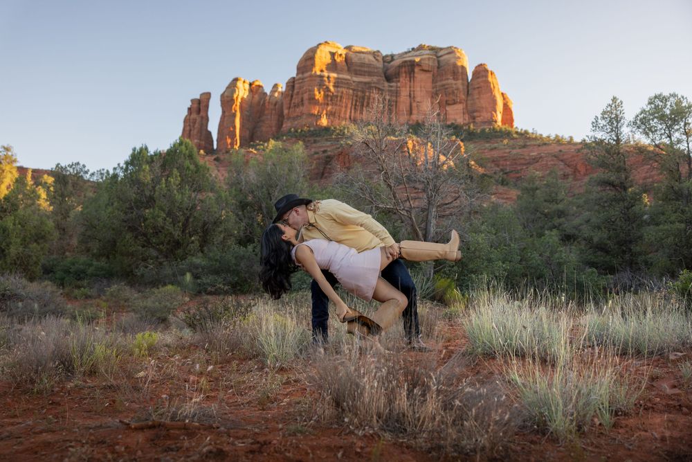 Man dipping woman romantically among Sedona red rock formations at sunset.