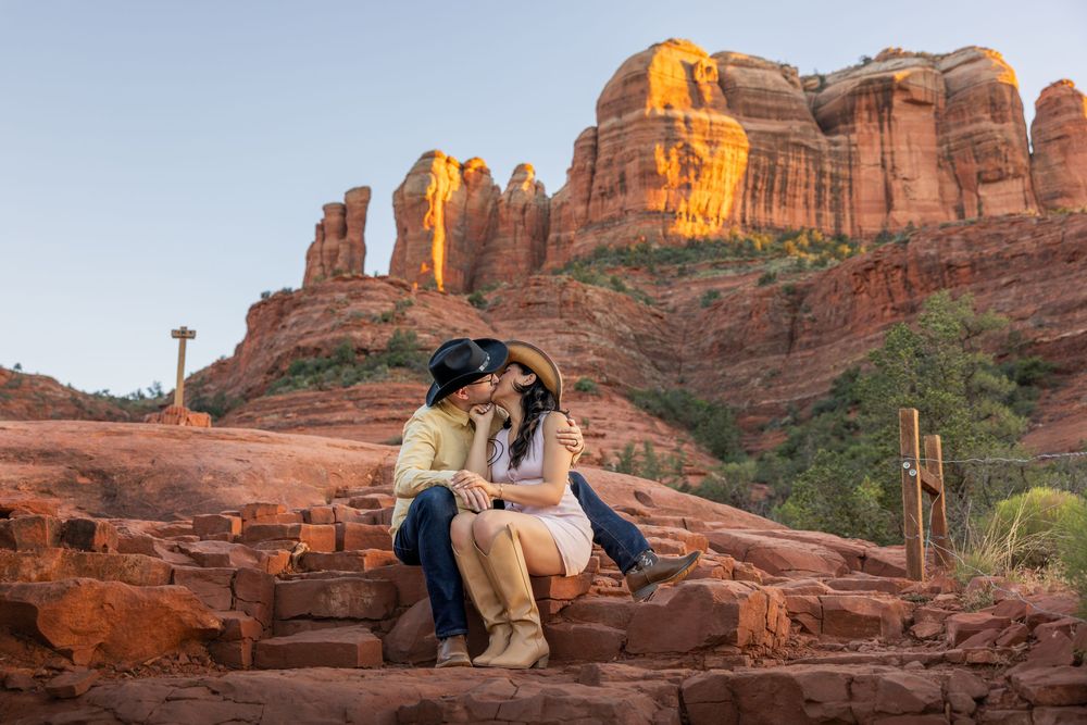 Romantic couple sharing a kiss on red rock steps with Cathedral Rock behind.