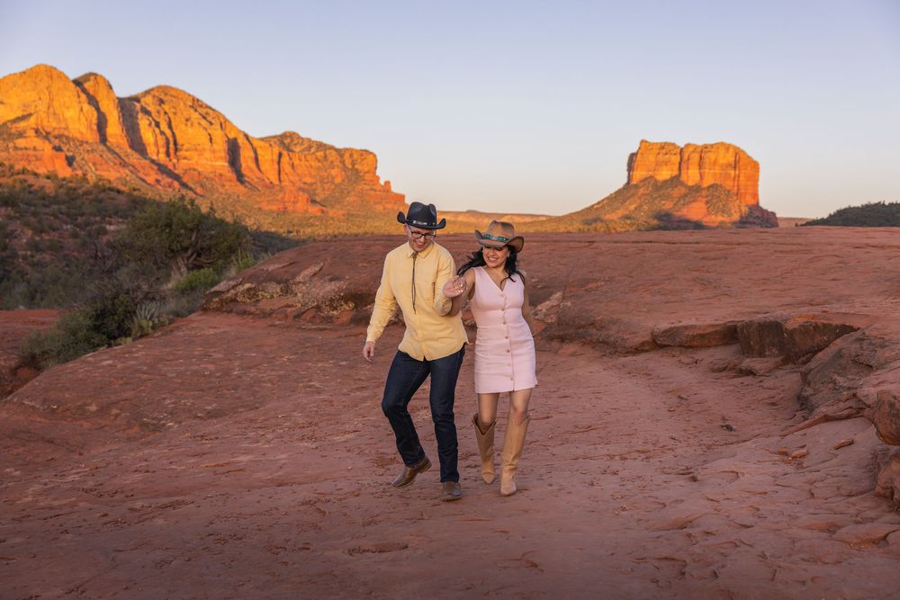 Happy couple walking hand-in-hand across red rock terrain in Sedona at sunset.