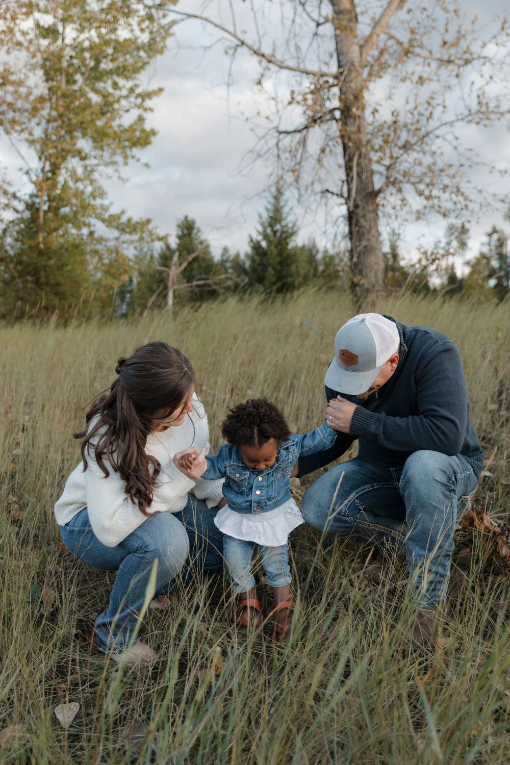 Family shares tender moment together in tall grass meadow during autumn.
