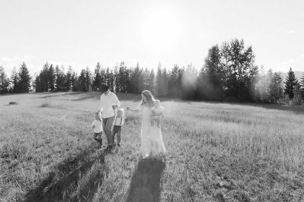 Black and white photo of people walking through a sunlit meadow surrounded by evergreen trees.