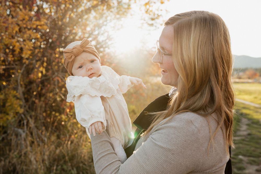 Parent holding baby against autumn sunset backdrop in rural field setting.