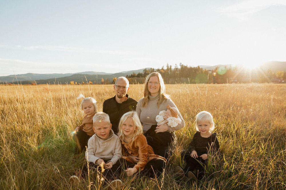 Family gathered together in autumn field with golden sunlight and mountains in background.