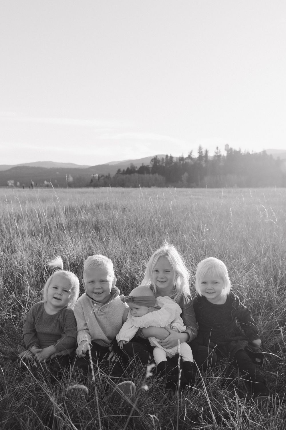 Family sitting together in a grassy field at sunset with mountains in the background.