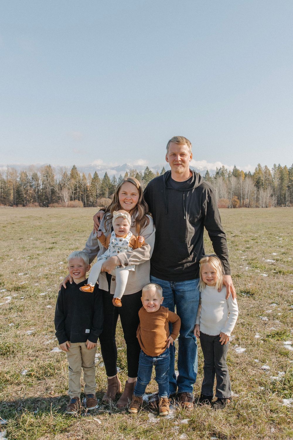 Family portrait in an open field with mountain ranges and forest in the background.