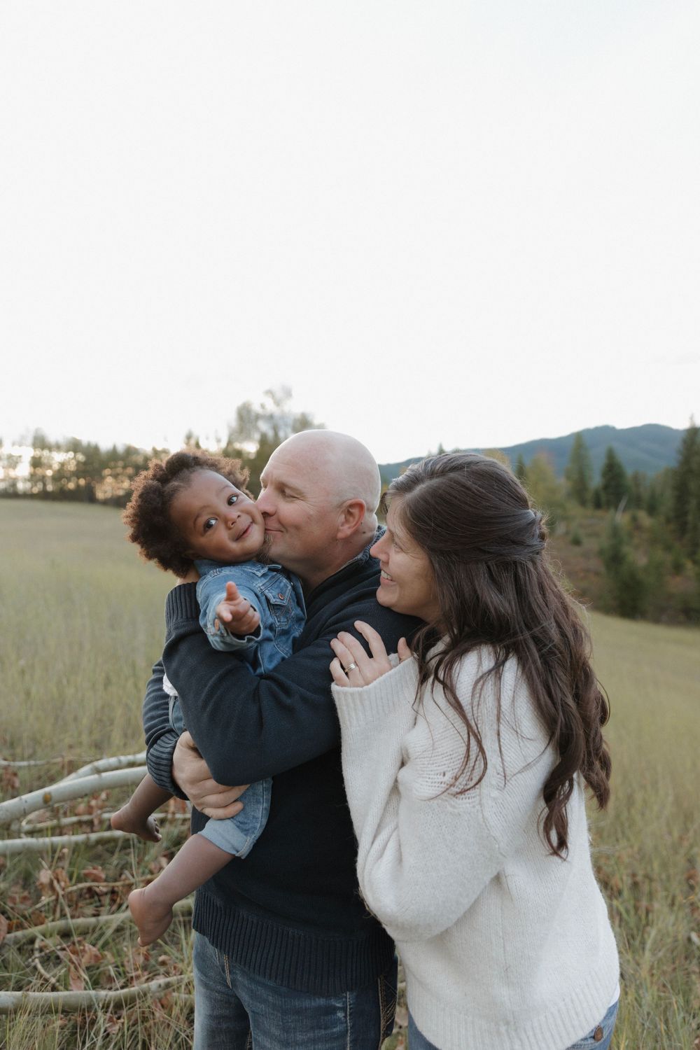 Family shares loving embrace in mountain meadow during golden hour.