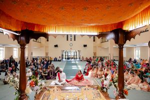 A traditional Sikh wedding ceremony taking place in a decorated indoor venue with guests seated on the floor.