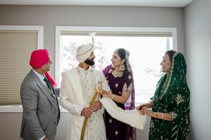 A group wearing traditional South Asian attire and turbans gather for a cultural ceremony indoors.