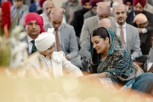 People seated together at a formal gathering wearing traditional cultural attire including a red turban and headscarf.