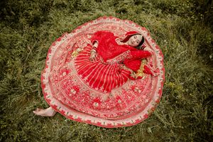 Overhead view of a woman in a flowing red traditional dress creating a perfect circular shape while lying on grass.