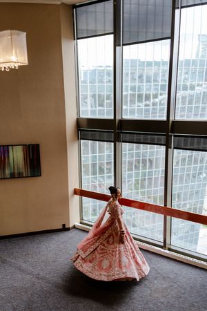A bride in a red lehenga twirls in front of large windows in a modern building.