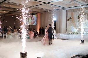 Indoor celebration with sparkling firework fountains and fog effects on a dance floor during an elegant event.