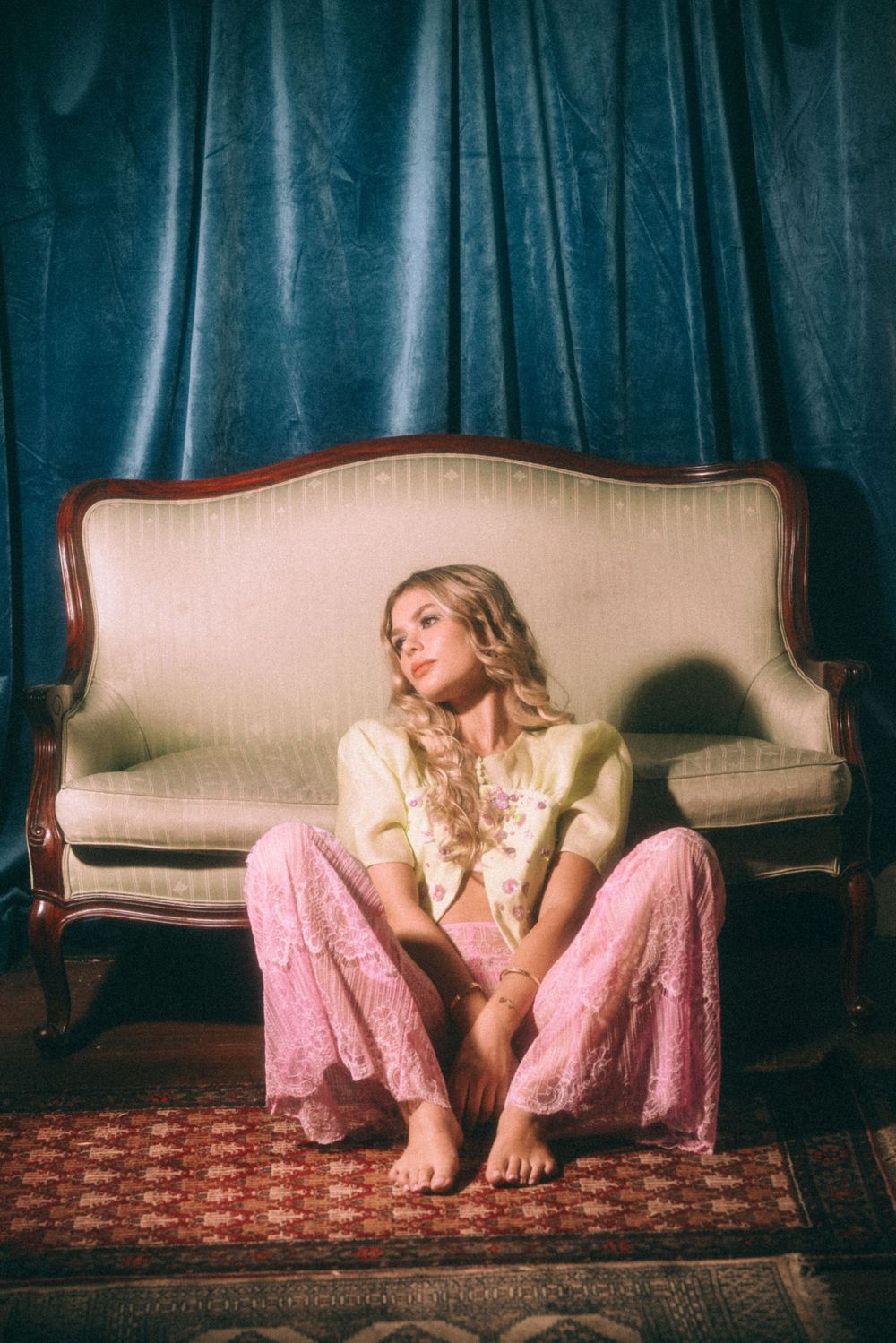 Dreamy vintage photo of a seated figure in pink pants against a teal velvet curtain backdrop.
